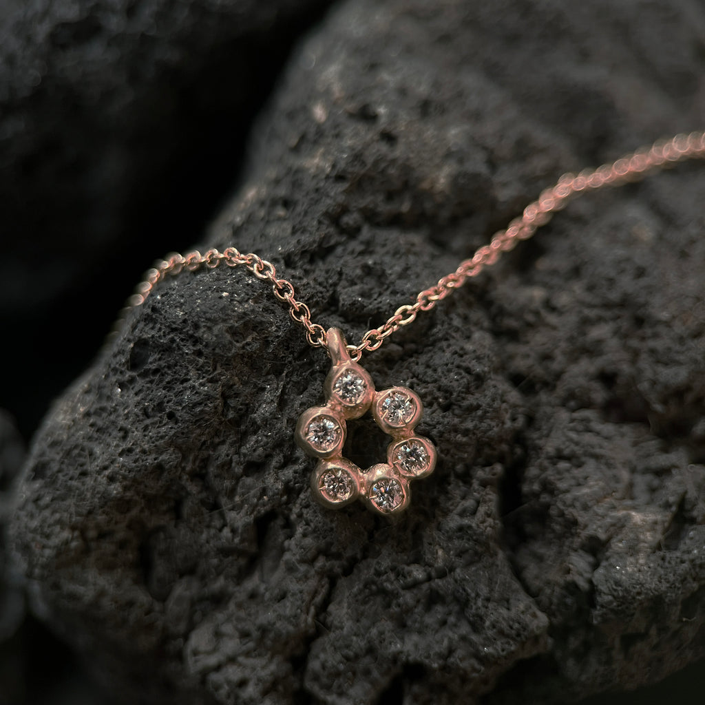 a pendant made of 6 small bud-like balls in an open oval shape, each one set with a diamond; shown in 14k rose