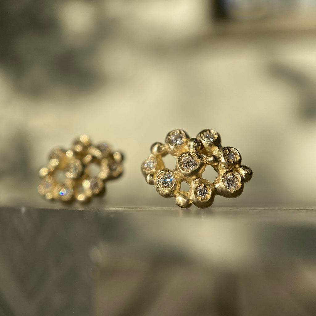 A stud made up of 8 larger, roundish balls ("buds") that each hold a diamond, and 6 tiny balls for accents; the overall feel is lacy because of the space between the various components; shown in 14k yellow; sitting outdoors in sunlight