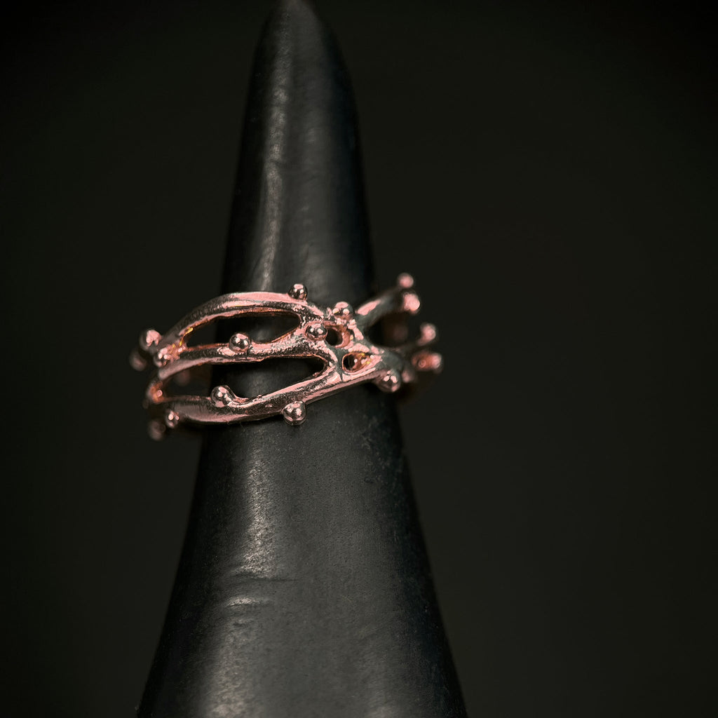 three intertwined slim branches with tiny bud-like balls scattered on the branches; shown in rose gold