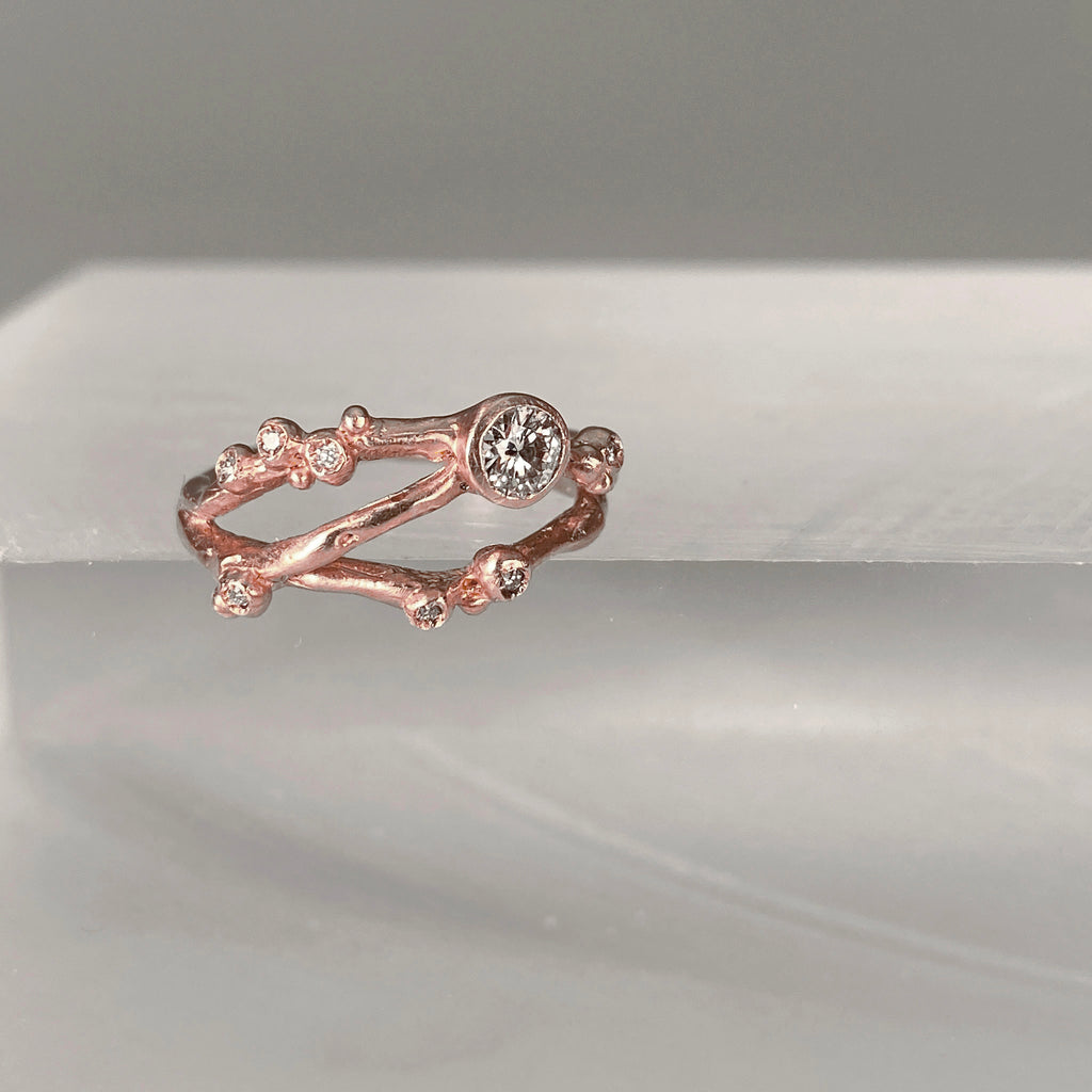 Organic, branch-like ring with three branches. Large off-center stone and seven tiny diamond buds. Shown in rose gold at slightly angled view.