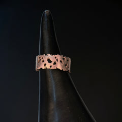 Flat-profile ring of 7 mm wide and 1 mm thick with jagged, organic cutouts and edges; shown in 14k rose gold with a satin finish