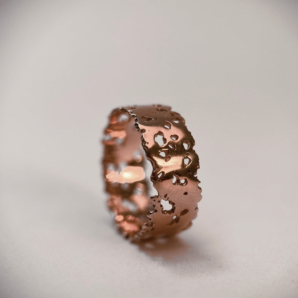 Flat-profile ring of 7 mm wide and 1 mm thick with jagged, organic cutouts and edges; shown in 14k rose gold with a polished finish