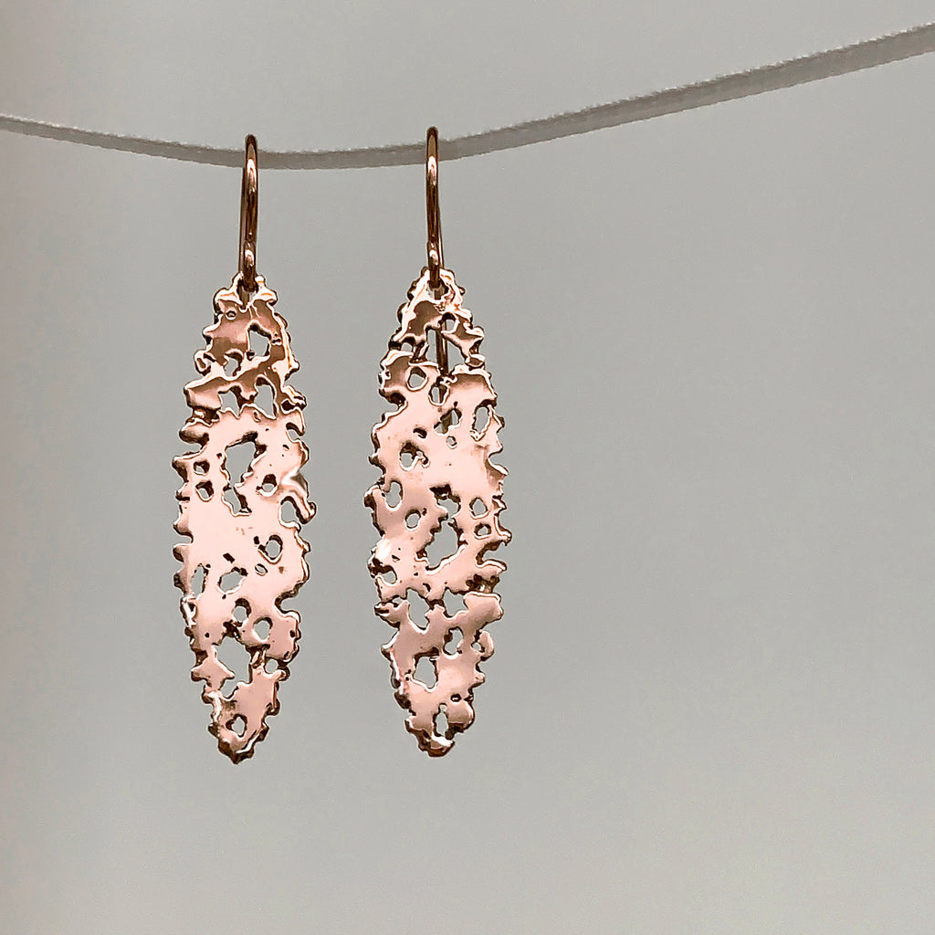 Shiny ellipse-shaped earring on wire, with organic holes, shown in rose gold.